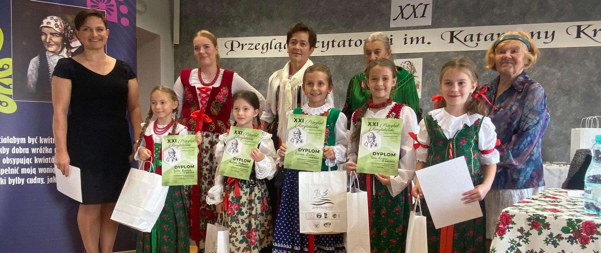 Uczestniczki konkursu w strojach galowych z dyplomami w ręku podczas nagradzania zwycięzców.