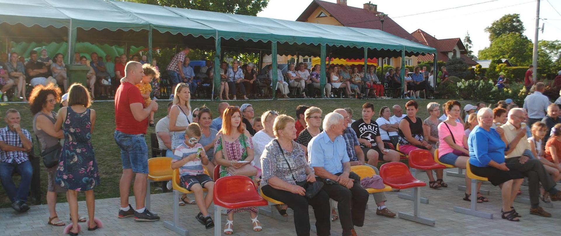 Zdjęcie przedstawia kilkadziesiąt osób siedzących na krzesełkach lub stojących i oglądających przedstawienia 