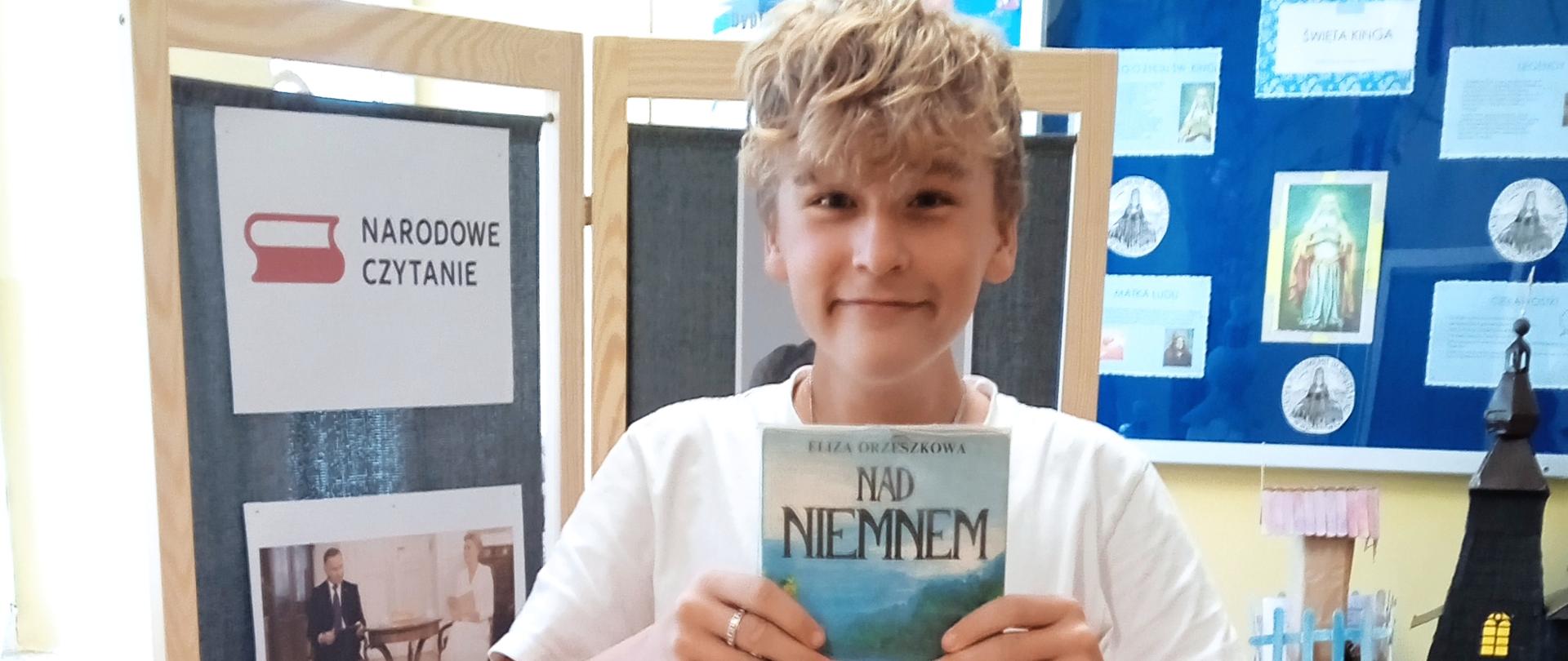 Uczeń trzyma w ręku książkę Elizy Orzeszkowej "Nad Niemnem"