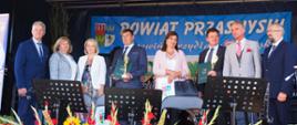 Wręczenie nagród dla najlepszych rolników w powiecie przasnyskim. Na scenie dożynkowej stoją samorządowcy Starosta Przasnyski, Sekretarz Gminy Przasnysz Bożena Rudzińska, Senator Jan Maria Jackowski wraz z nagrodzonymi rolnikami z terenu gminy Przasnysz.