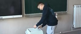Uczeń wrzuca kartę ze swoim głosem do urny wyborczej