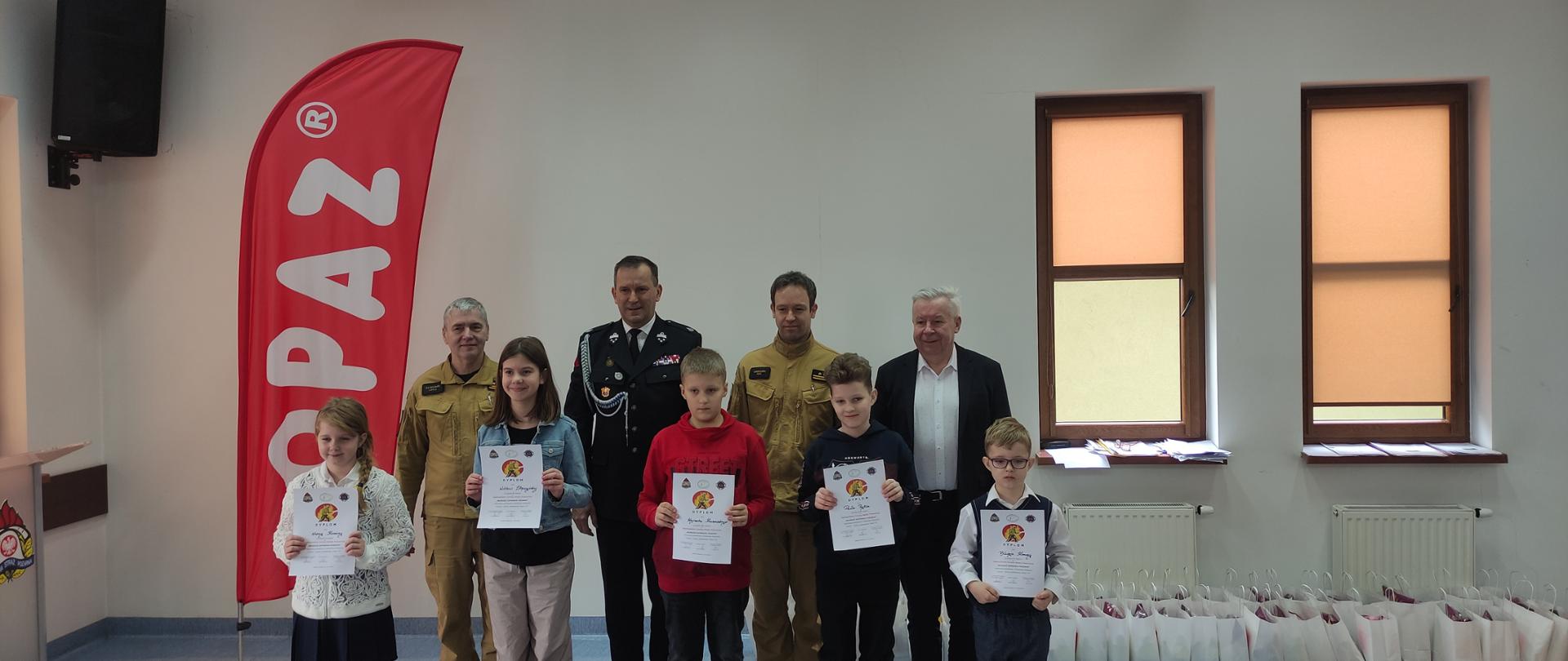 Fotografia grupowa wykonana w siedzibie PSP w Sokołowie Podlaskim, na zdjęciu nagrodzeni uczestnicy, trzymają w dłoniach dyplomy, oraz przedstawiciele Straży Pożarnej i Starostwa Powiatowego w Sokołowie Podlaskim.