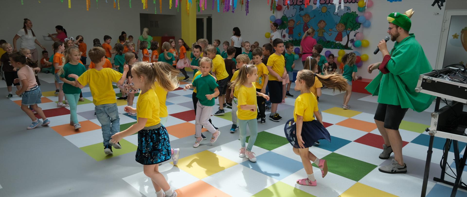 Dzieci bawią się w kolorowej sali a przygrywa im dj przebrany za żabę.