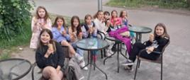 Dzieci siedzą przy stolikach ustawionych na kostce i jedzą lody