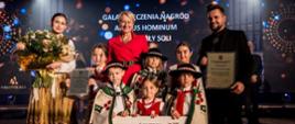 Przedstawiciele Stowarzyszenia Mała Armia Janosika (trzy osoby dorosłe i sześcioro dzieci w strojach regionalnych) odbierają nagrodzę Lider Pozarządowej Małopolski Kryształy Soli 2023