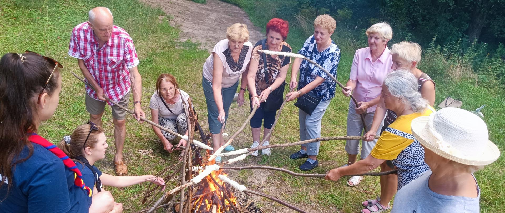 członkowie klubu senior+ przygotowujący nietypowe (pieczone na kijach) podpłomyki