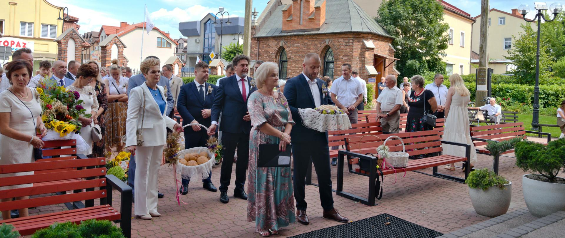 Uczestnicy uroczystości, mszy świętej, stoją przed wejściem do kościoła z wieńcami i koszami dożynkowymi.