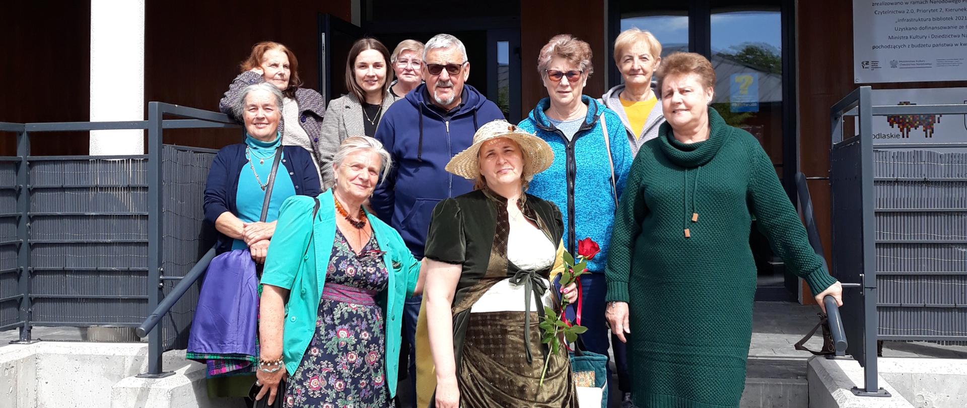 Członkowie Klubu Senior+ stojący przed biblioteką w Dąbrowie Białostockiej wraz z Panią Beatą Choińską z Muzeum im. Marii Konopnickiej w Suwałkach