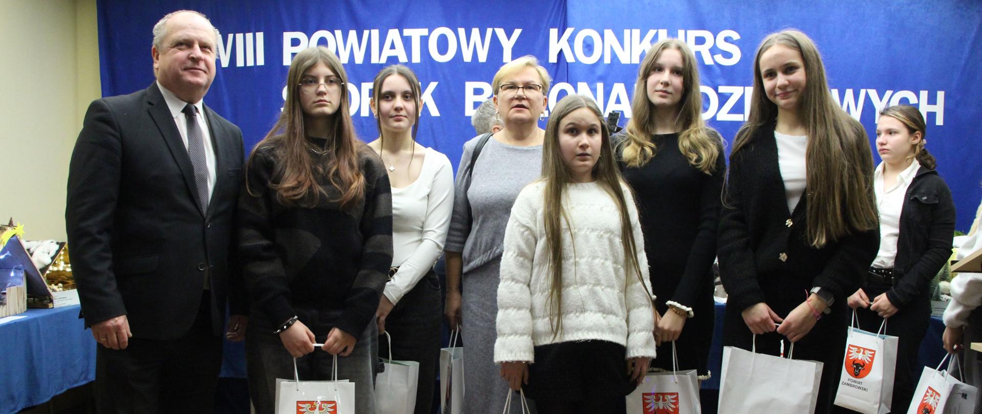 Zdjęcie przedstawia laureatów konkursu, którzy trzymają w dłoniach nagrody (6 osób). Od lewej strony Pan Robert Maciej Rosiak Wicestarosta Zambrowski, w środku kobieta ubrana w kostium w kolorze szarym.
