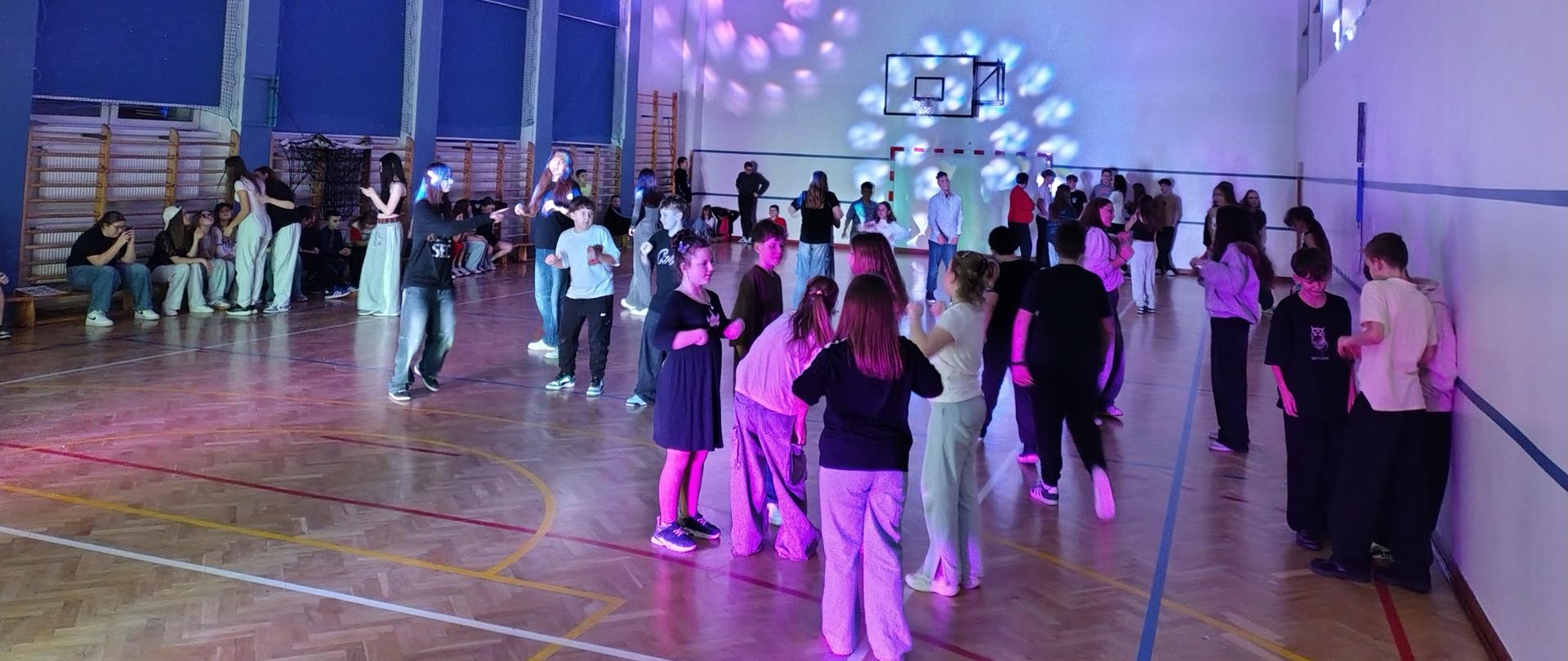 Uczniowie klas IV - VIII bawią się w rytm muzyki na sali gimnastycznej podczas dyskoteki karnawałowej