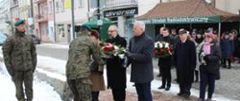 Delegacja Powiatu Przasnyskiego ze Starostą Krzysztofem Bieńkowskim na czele podaje kwiaty oraz znicz żołnierzowi. Zdjęcie wykonane pod pomnikiem straconych przez Niemców żołnierzy Armii Krajowej - rynek w Przasnyszu.