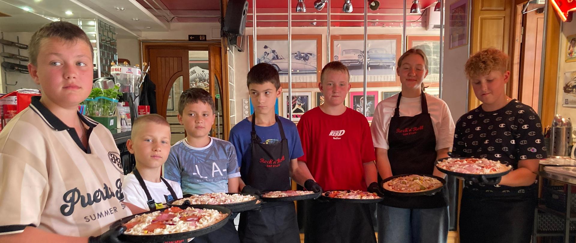 Uczniowie stoją w restauracji „Rock'n'Roll”, prezentują samodzielnie przygotowane pizze