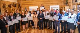 Zdjęcie grupowe: Wójtowie i burmistrzowe trzymający symboliczne promesy. w centralnej części zdjęcia marszałek Małopolski Witold Kozłowski, senator Jan Hamerski, poseł Anna Paluch, poseł Patryk Wicher oraz radny województwa Stanisław Barnaś