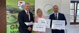 trzy osoby dwóch mężczyzna i kobieta na tle tablic informacyjnych- Gminy Mokobody i WFOŚiGW