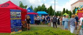 Festyn Profilaktyczno Zdrowotny w ogrodach przasnyskiego szpitala. Zdjęcie przedstawia uczestników Festynu korzystających z darmowych porad i badań. W tle stanowiska ciechanowskiej Państwowej Szkoły Zawodowej imienia Ignacego Mościckiego.