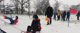 Zabawy na śniegu - dzieci pokonują tor przeszkód w zaprzęgu