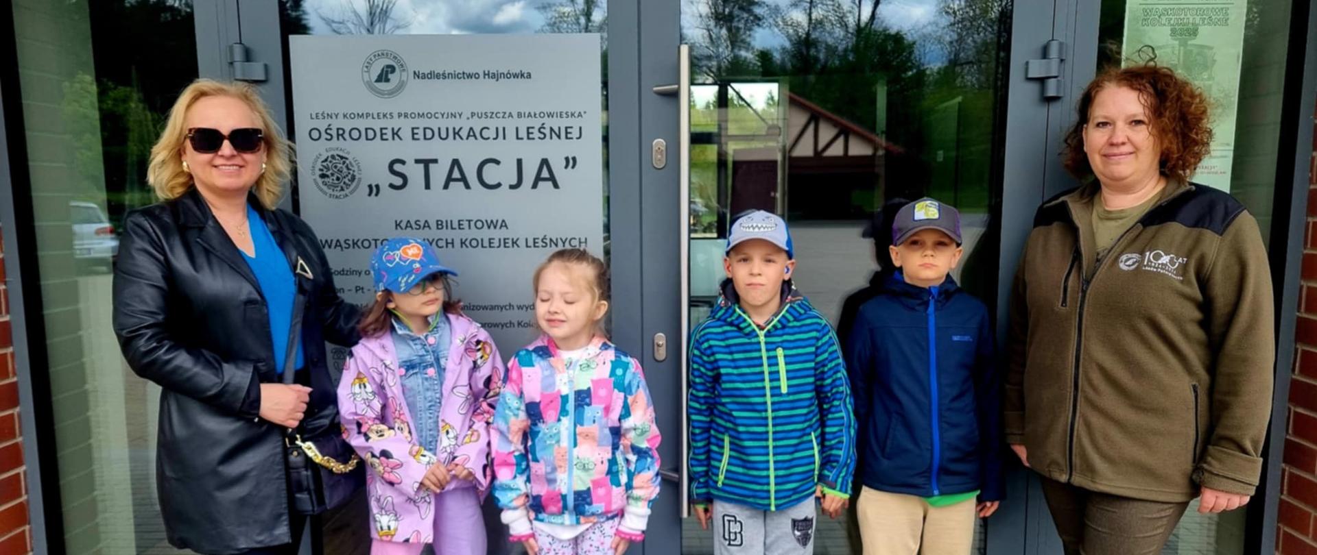 Przedszkolaki pozują do zdjęcia przy wejściu do Ośrodka wraz w Panią Dyrektor i pracownikiem Nadleśnictwa Hajnówka 