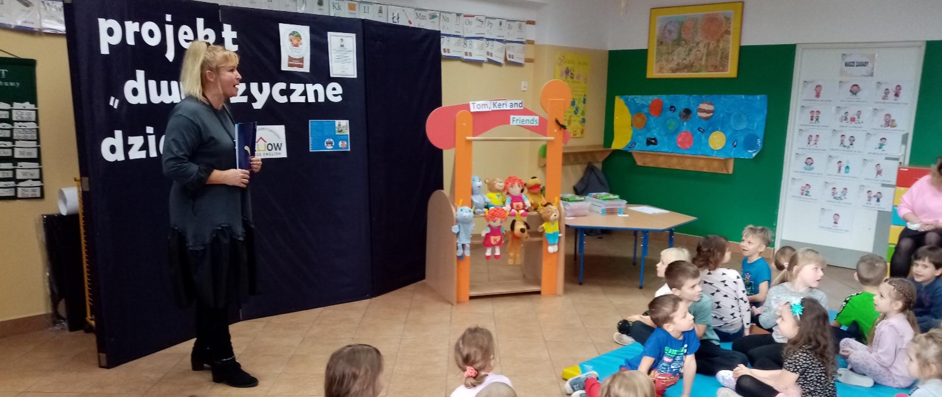 Kobieta stoi i przemawia do dzieci siedzących na podłodze na materacach