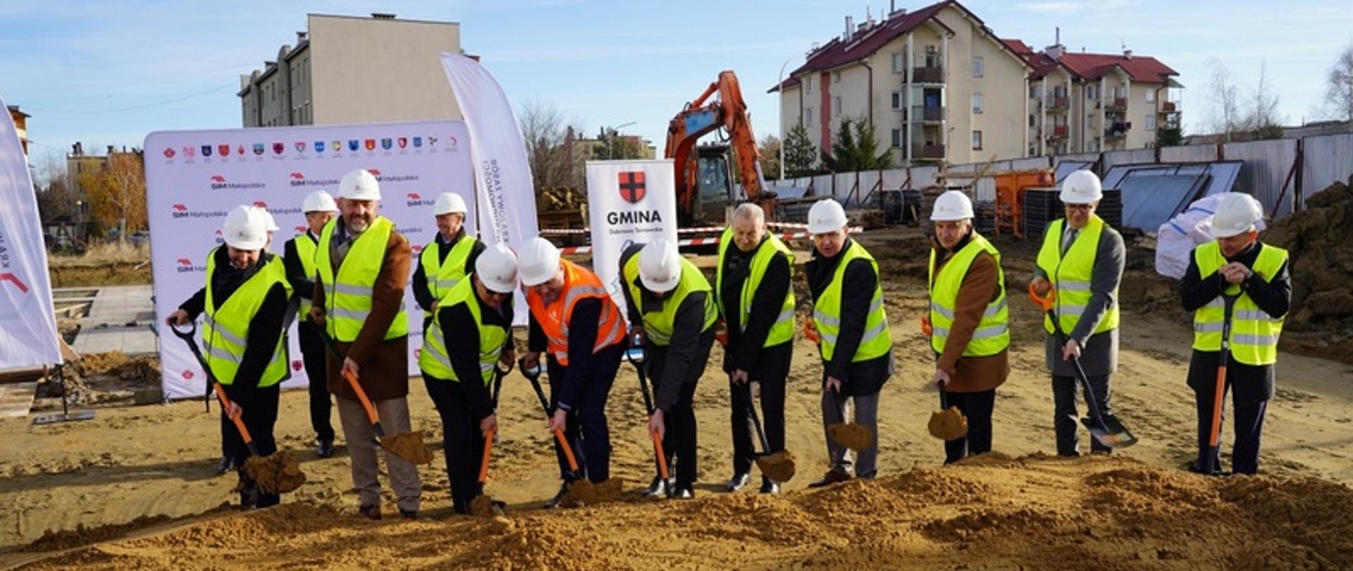Uczestnicy wydarzenia dokonują symbolicznego wbicia łopaty na placu budowy