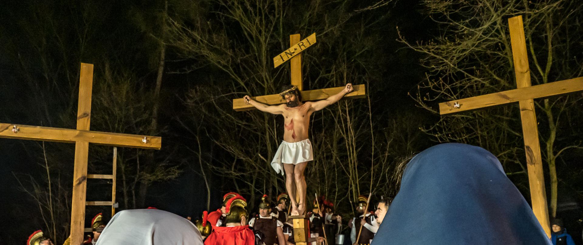 Zdjęcie przedstawia trzy, ustawione obok siebie krzyże, otoczone przez uczestników misterium i aktorów w strojach rzymskich legionistów. Na stojącym w centrum krzyża znajduje się aktor odgrywający Chrystusa.