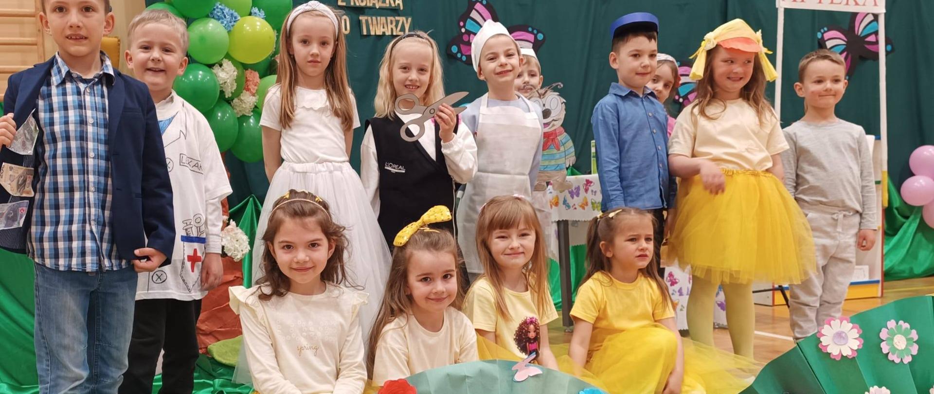 Grupa uśmiechniętych dzieci w pięknych strojach - dziewczynki w żółtych spódniczkach, białych bluzeczkach, chłopcy w fartuchach lekarzy .