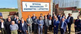 Zdjęcie przedstawia licznie przybyłych gości na uroczystość rozpoczęcia budowy Laboratorium Politechniki Warszawskiej w Przasnyskiej Strefie Gospodarczej. W tle budowa w trakcie oraz tablica z napisem "Wydział Mechaniczny Energetyki i Lotnictwa".