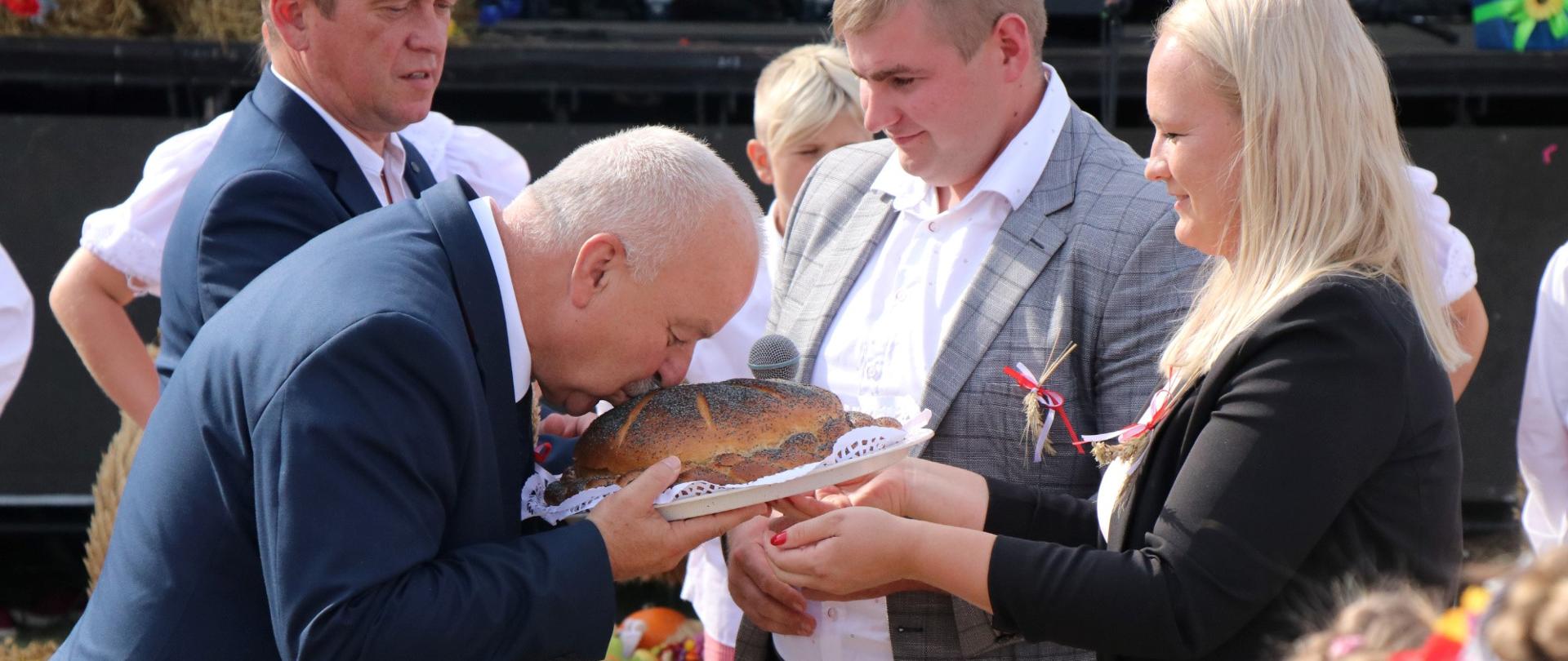 Starosta i Starościna dożynek przekazują Burmistrzowi chleb. Burmistrz całuje chleb.