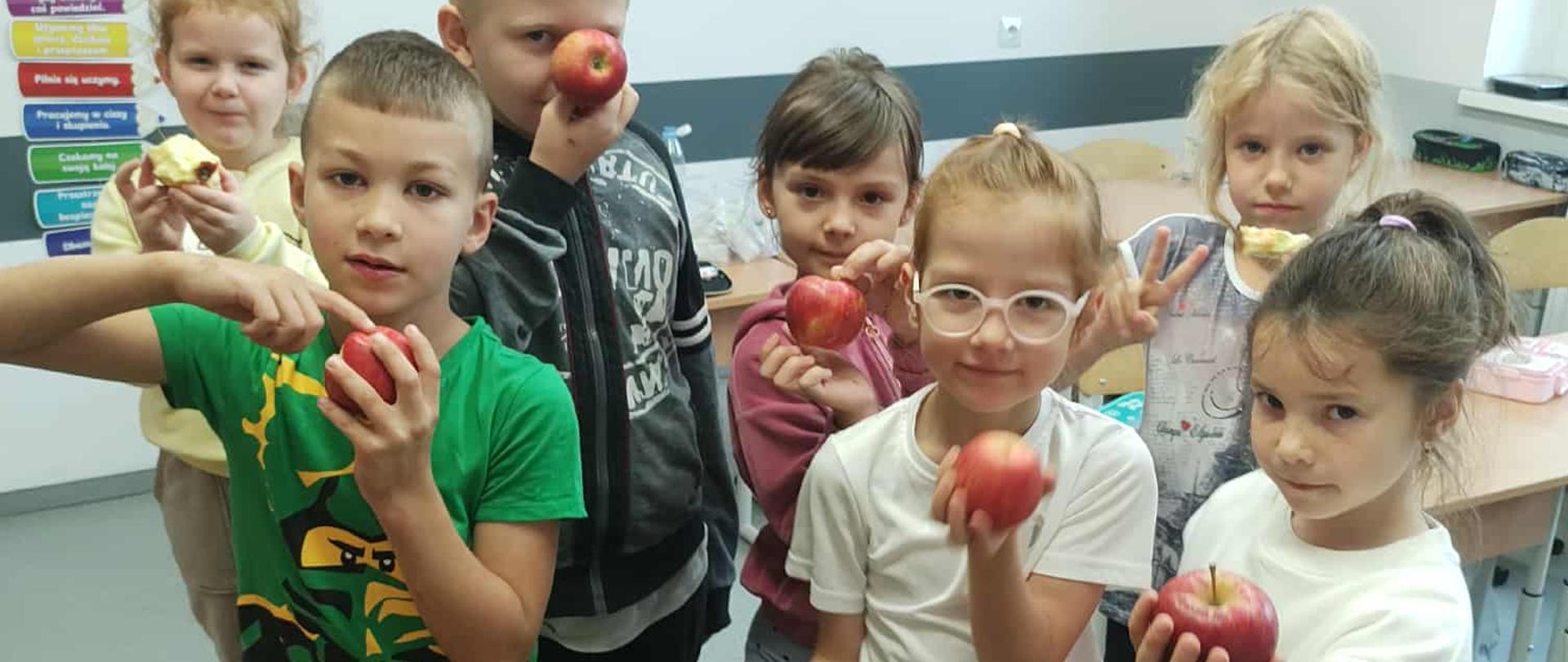 Siedmioro uczniów klasy pierwszej - dwóch chłopców i pięć dziewczynek pozuje z jabłkami w dłoniach.