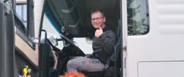 Uczeń siedzi w ciężarówce na fotelu kierowcy, z otwartymi drzwiami, obok których stoi człowiek ubrany w strój lwa