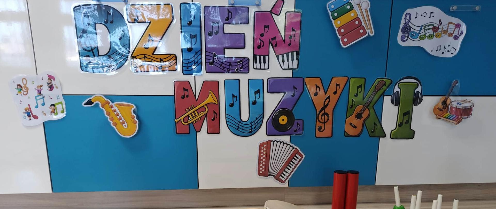 Na zdjęciu widać rozłożone instrumenty muzyczne: marakasy , tamburyno, dzwoneczki. W tle widnieje kolorowy napis "Dzień Muzyki".