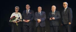 Pięć osób elegancko ubranych, czterech mężczyzn oraz jedna kobieta. Kobieta trzyma bukiet kwiatów.