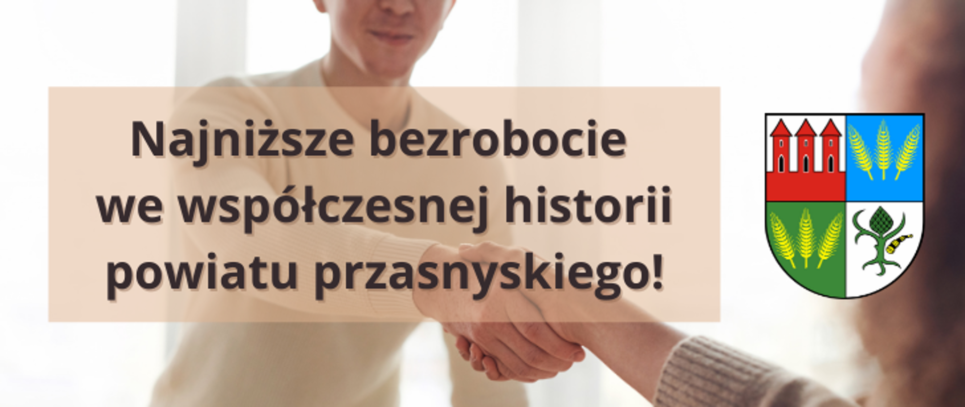 Grafika przedstawia informację o najniższym w historii Powiatu Przasnyskiego poziomie bezrobocia. W tle uścisk dłonie młodego mężczyzny oraz osoby wyciągającej dłoń spoza kadru. Po lewej stronie herb Powiatu Przasnyskiego, po prawej napis "Najniższe bezrobocie we współczesnej historii powiatu przasnyskiego!".
