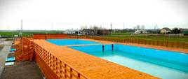 Zdjęcie przedstawia jedną z niecek oraz drewnianą konstrukcję kompleksu basenów otwartych w Przasnyszu. Basen przed oddaniem do użytku na wiosnę 2023.