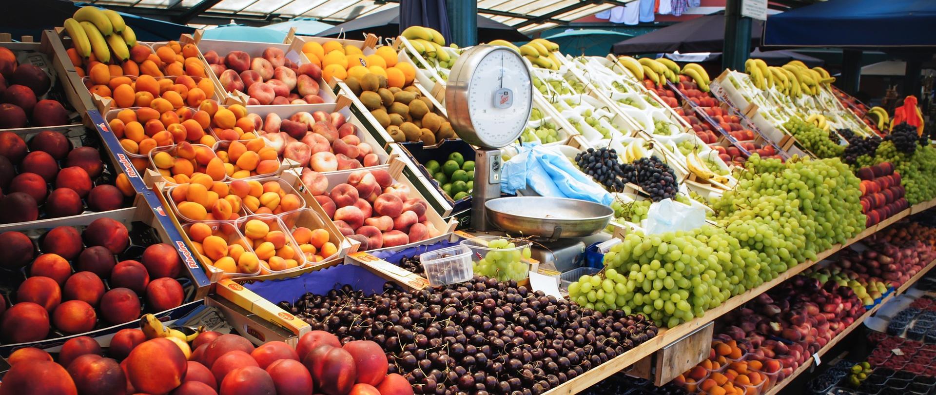 Na zdjęciu widok straganu z owocami. Stragan zlokalizowany jest wewnątrz hali targowej.