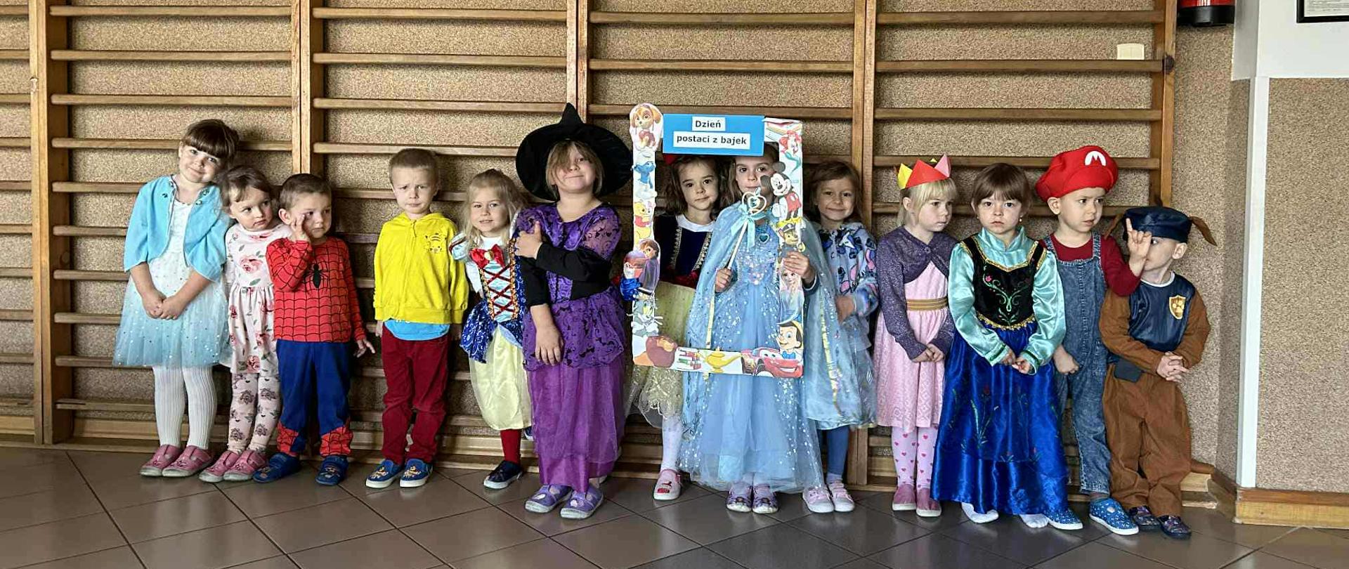 Trzynaścioro dzieci z Oddziału Przedszkolnego B pozuje do wspólnego zdjęcia. Dzieci przebrane są bajkowe stroje, między innymi: księżniczek, czarodziejki, Spider Mana.
