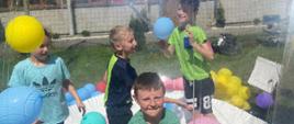 Dzieci bawią się w dużej przeźroczystej kuli, w której podrzucają kolorowe balony