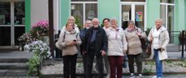 siedem kobiet i jedne mężczyzna stojący w środku pozują do zdjęcia na tle zielonego budynku 