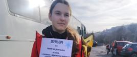 Uczennica naszej szkoły pozuje w stroju narciarskim z medalem, pucharem i dyplomem zdobytym w Zawodach narciarskich o Puchar Wójta Gminy Łabowa, w tle autokar