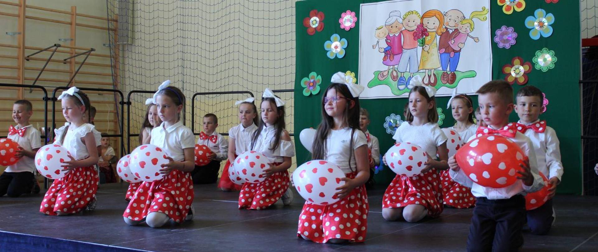 Na scenie dzieci trzymające balony uczestniczą w przedstawieniu