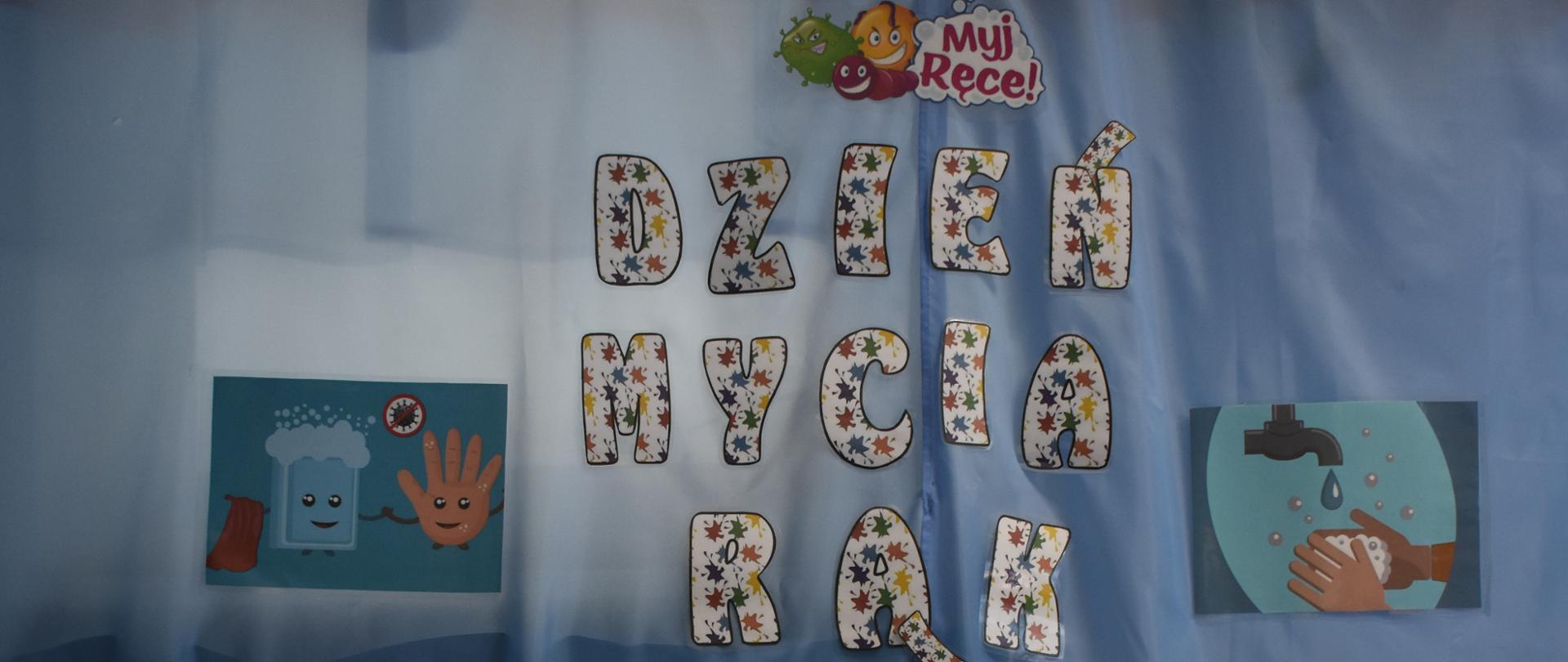 Zdjęcie przedsawia dziewczynkę, która siedz przy stoliku, przed nią lezy biały brystol z narysowanym kranem. Dziecko odbija rękę pomalowaną farbą. Nad dziewczynką wisi napis Dzień Mycia Rąk