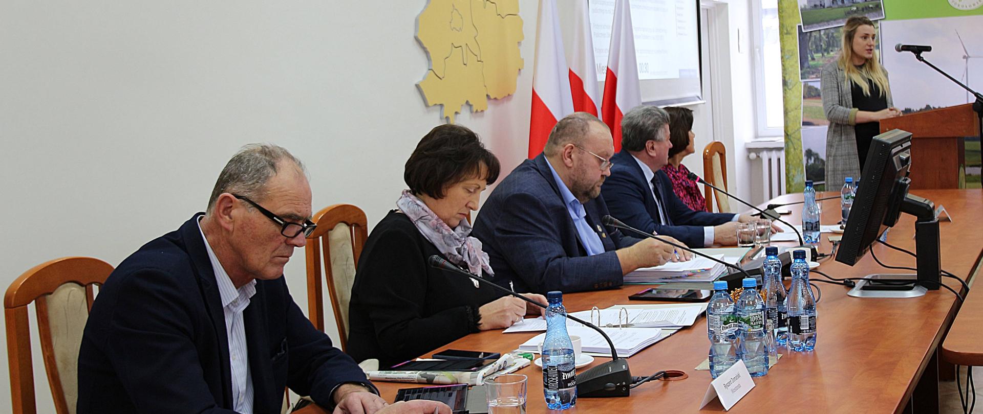 Na zdjęciu przy stole od lewej wicestarosta, starosta, przewodniczący Rady oraz dwóch członków Zarządu, przy mównicy z prawej strony stoi mieszkanka powiatu, która opisuje niedogodności dotyczące drogi. Zarząd słucha i robi notatki.