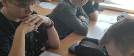 Dwóch chłopców siedzi przy stole i czyta treść leżących przed nimi kartek.
