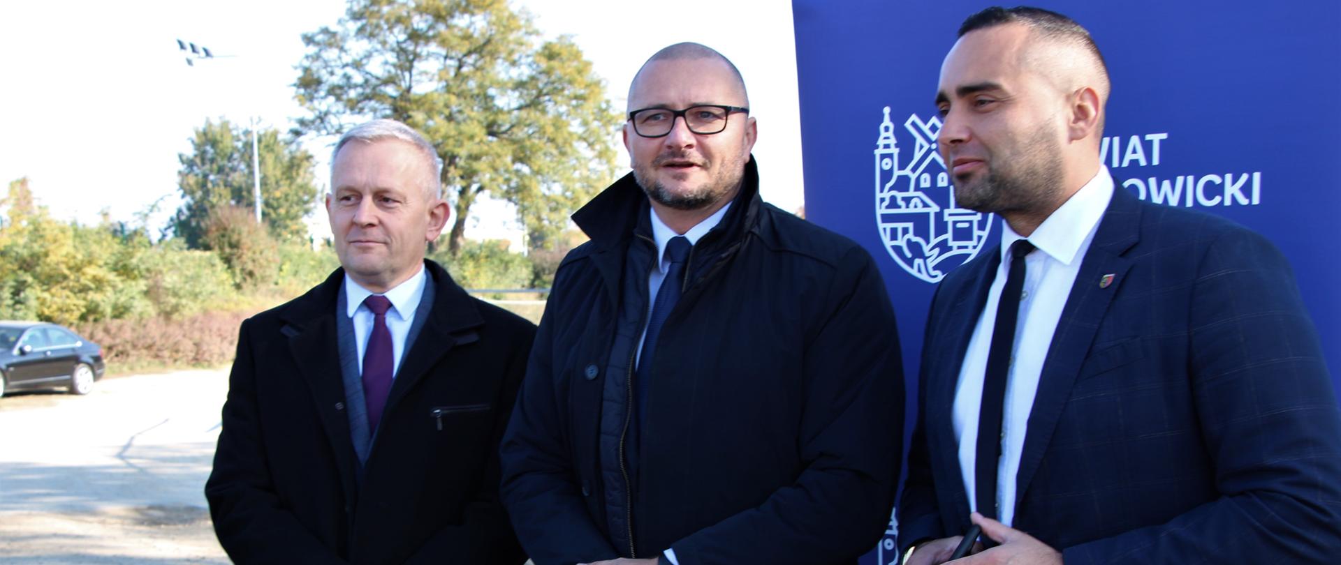 Trzech mężczyzn stoi z dokumentami w rękach. 