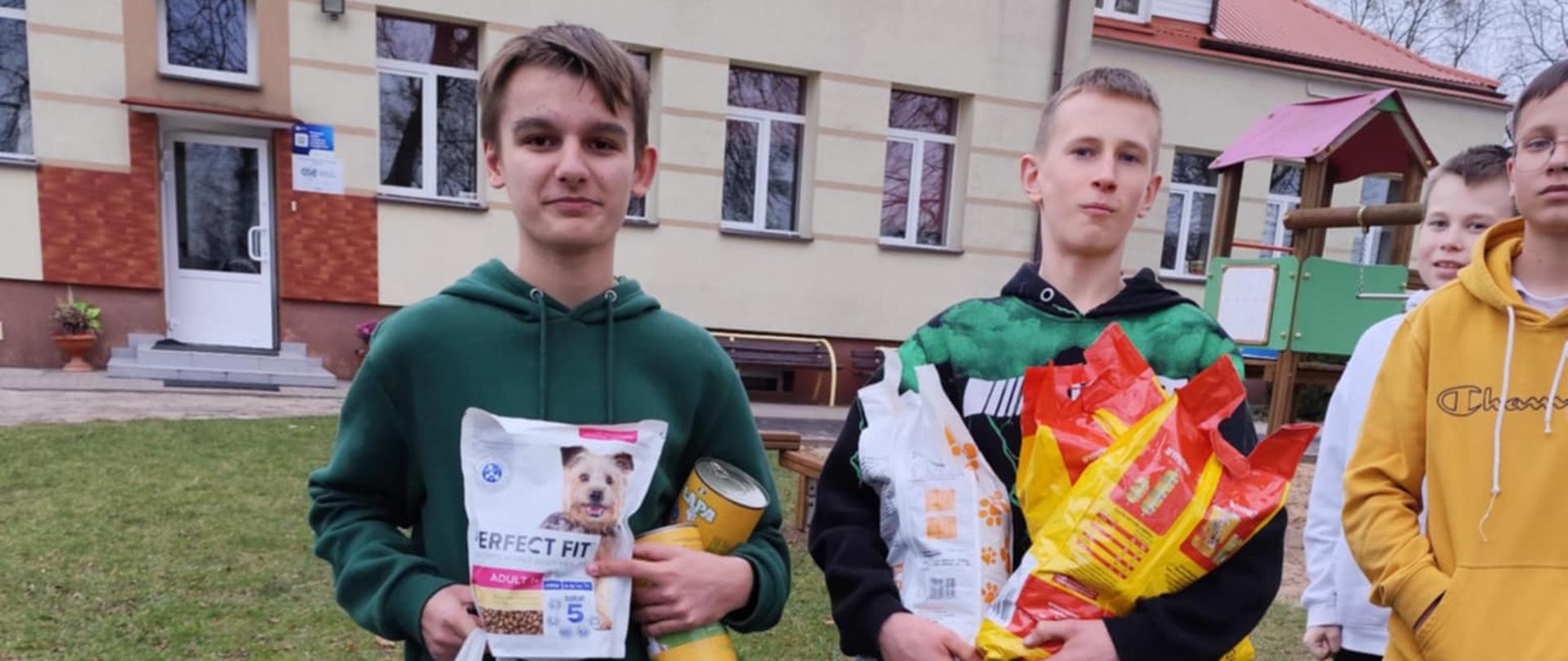 Czworo chłopaków pozuje do zdjęcia. Dwoje z nich ma w rękach paczki z karmą dla psów.