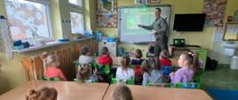 Dzieci siedzą przy ławkach szkolnych, zwrócone są twarzą do tablicy multimedialnej, na której leśniczy pan Przemysław Nosal wyświetla prezentację na temat ptaków zimujących w Polsce