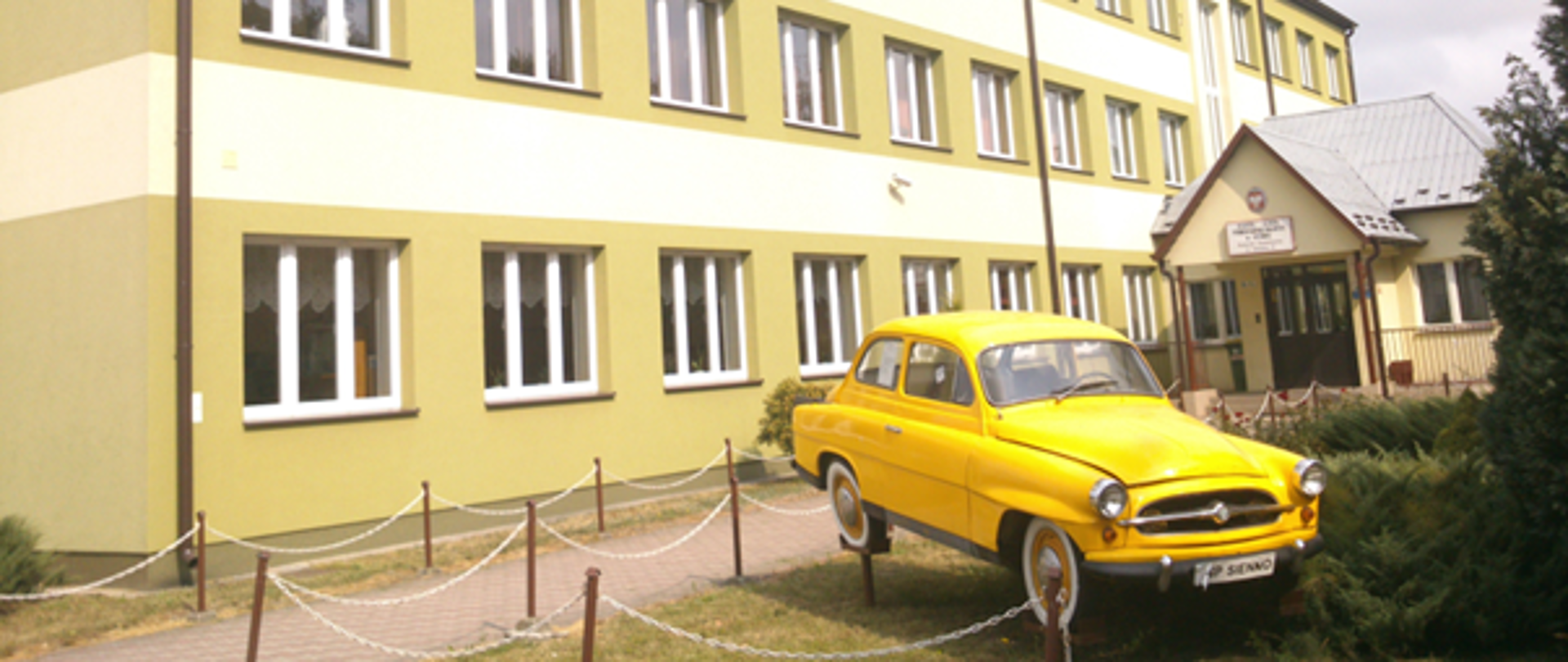 Budynek Zespołu Szkół Technicznych w Siennie. Przed budynkiem stoi żółty samochód.