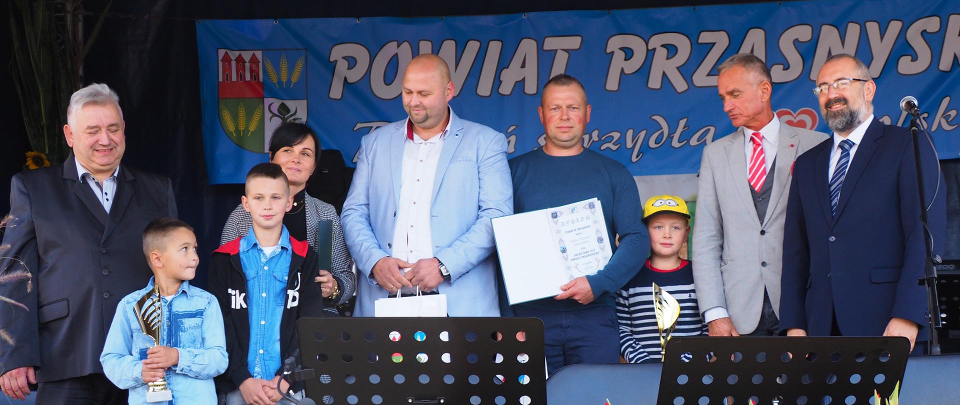 Wręczenie nagród dla najlepszych rolników w powiecie przasnyskim. Na scenie dożynkowej stoją Senator Jan Maria Jackowski, Starosta Przasnyski Krzysztof Bieńkowski, Dyrektor Wydziału Rolnictwa i Środowiska Powiatu Przasnyskiego Jacek Tomczak wraz z nagrodzonymi rolnikami z terenu gminy Chorzele.
