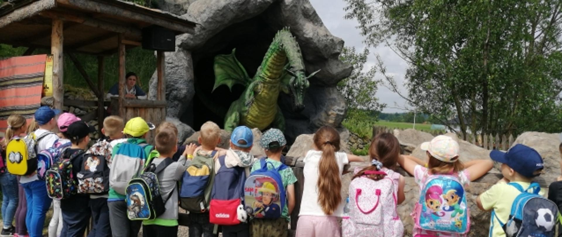 Zdjęcie przedstawia grupę dzieci patrzących na dużego, zielonego smoka.