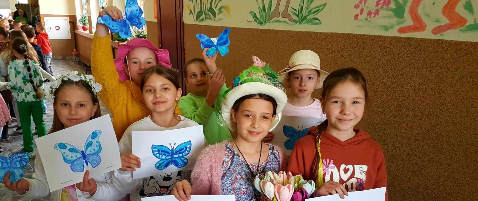Uczniowie w barwach wiosennych z pracami plastycznymi zawierającymi niebieskie motyle- symbol solidarności z osobami z Zespołem Downa