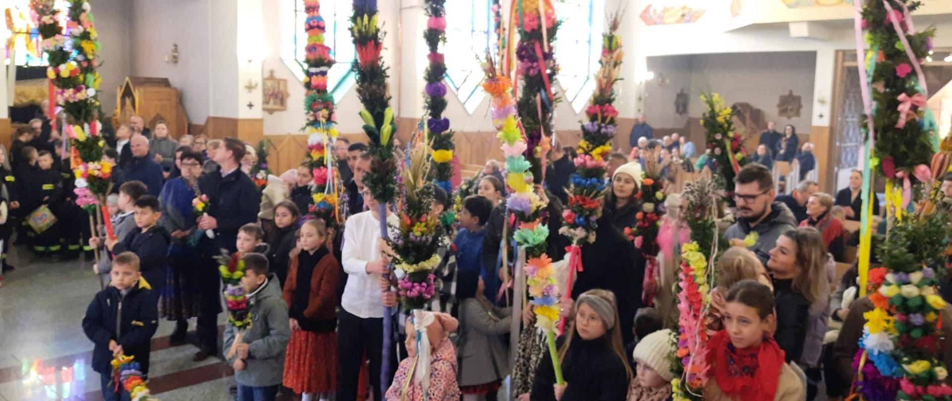Zdjęcie przedstawia uczestników z palmami pozujących do zdjęć przed ołtarzem w kościele parafialnym w Rokicinach Podhalańskich